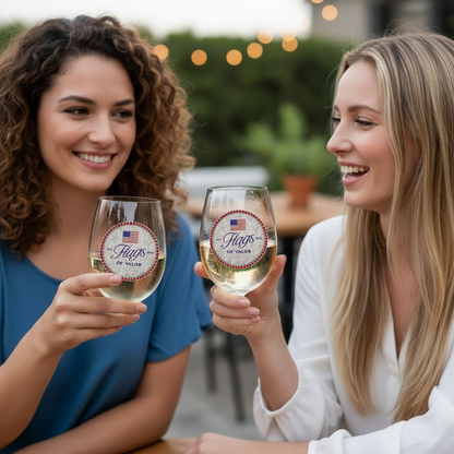 Two women holding wine glasses with 'Flags of Valor' branding outdoors.
